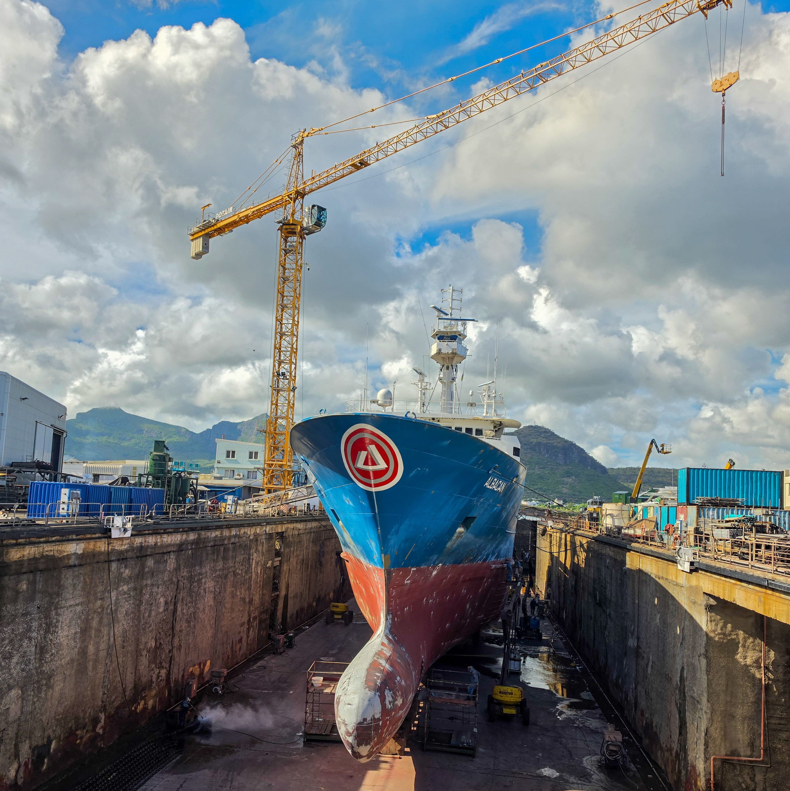 Cargo ship hull and propeller in a drydock during repair, with a tower crane overhead